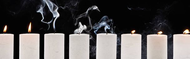 burning and extinct white candles with smoke on black background, panoramic shot - Fotó, kép