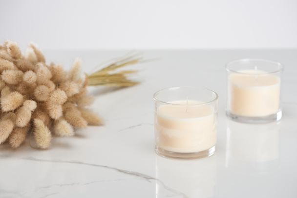 selective focus of fluffy bunny tail grass and white candles in glass on marble white surface - Foto, Imagen