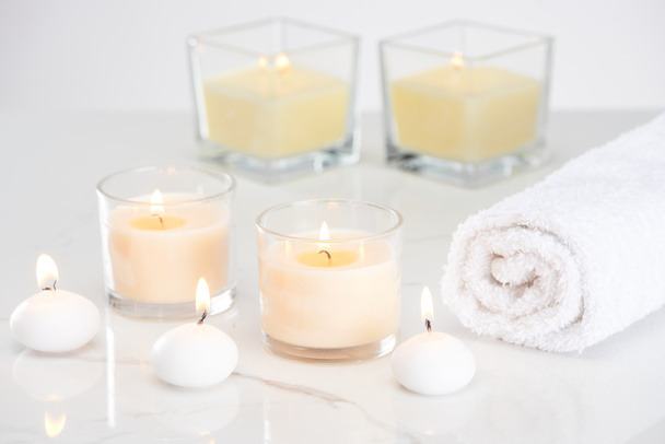 brennende weiße Kerzen im Glas und gerolltes Handtuch auf marmorweißer Oberfläche - Foto, Bild