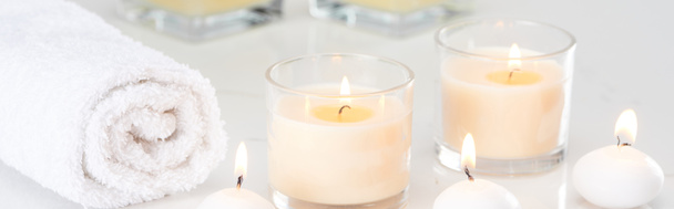 brennende weiße Kerzen im Glas und gerolltes Handtuch auf marmorweißer Oberfläche, Panoramaaufnahme - Foto, Bild