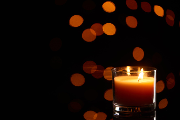brennende Kerze, die im Dunkeln mit Bokeh-Lichtern auf dem Hintergrund glüht - Foto, Bild
