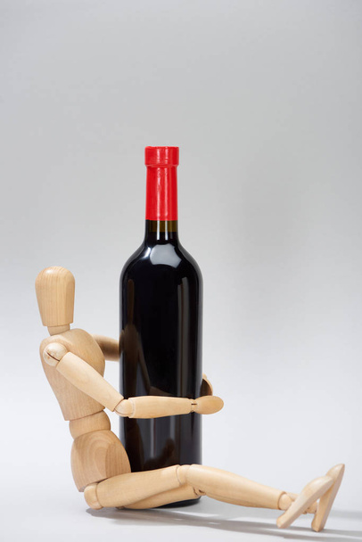 Holzpuppe neben Flasche Rotwein auf grauem Hintergrund - Foto, Bild