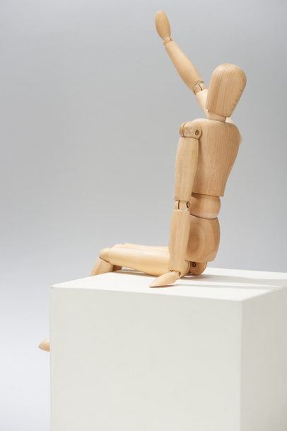 Wooden puppet with outstretched hand on white cube on grey background - 写真・画像