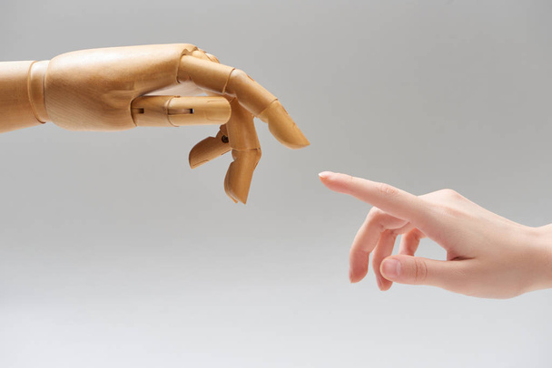 Vista recortada de la mujer y la mano de la muñeca de madera tirando de los dedos entre sí aislado en gris
 - Foto, Imagen