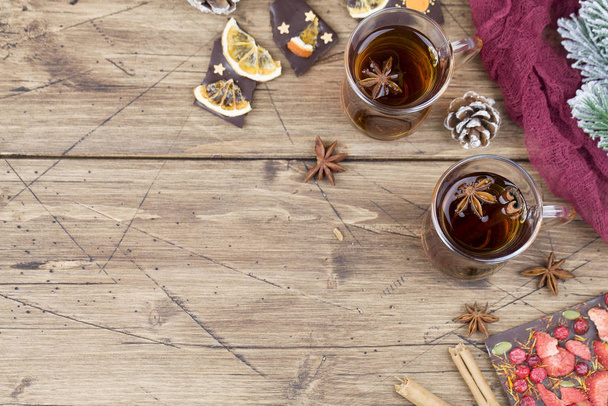 Winter hot tea with cinnamon, anise, chocolate with fruit, cone and christmas tree branch on wood brown background. - Foto, Imagem