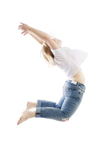 Een jonge blonde vrouw in jeans en een wit T-shirt springen emotioneel op. Zijaanzicht.Geïsoleerd op een witte achtergrond. - Foto, afbeelding