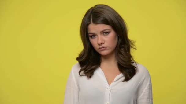 Upset young woman with brunette hair in blouse looking at camera with frustrated resentful expression, feeling depressed offended, is about to cry. indoor studio shot isolated on yellow background - Imágenes, Vídeo