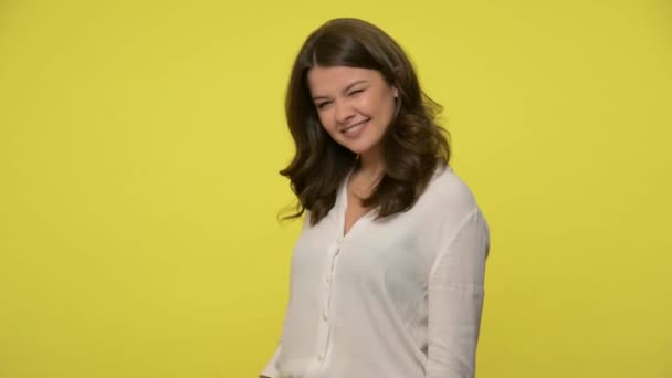 Devious attractive woman with brunette hair in blouse smiling sly mysteriously and mulling over cunning plan, sneaky scheming idea, villain cheat. indoor studio shot isolated on yellow background - Filmagem, Vídeo