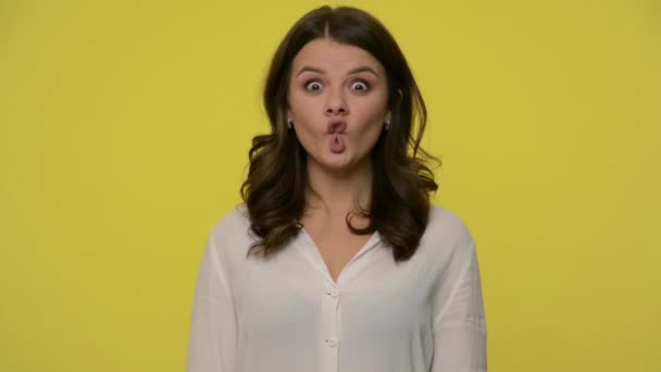 Funny amusing woman with brunette hair in blouse making fish face with lips and amazed big eyes, looking sides, showing comic ridiculous grimace, having fun. studio shot isolated on yellow background - Imágenes, Vídeo