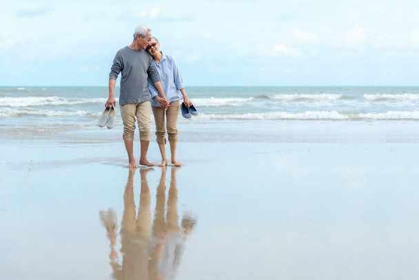 Lifestyle aziatisch senior koppel gelukkig wandelen knuffel en ontspannen op het strand. Toerisme ouderen familie reizen vrije tijd en activiteit na pensionering in vakanties en zomer. - Foto, afbeelding
