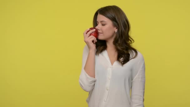 Attractive slim woman biting red apple and eating, her eyes closed from pleasure and satisfaction, concept of delicious fruits as healthy diet food. indoor studio shot isolated on yellow background - Video