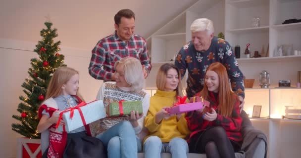 Grote familie geven elkaar kerstcadeaus zittend op de bank, kerstboom familie idylle - Video