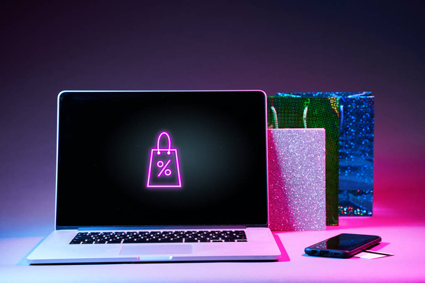 Laptop, dárkový balíček, telefon a platební karta na stole v moderních neonových barvách. - Fotografie, Obrázek