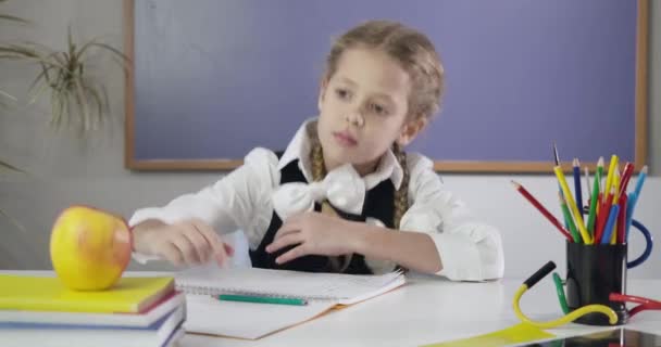 Charming Caucasian schoolgirl writing in exercise book, biting apple and showing thumb up. Happy female student doing homework. Education concept, intelligence. Cinema 4k ProRes HQ. - Záběry, video