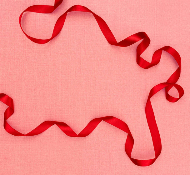 Red wavy ribbon on pink background. Holiday decoration. Valentine's Day decoration congratulation frame. - Photo, image