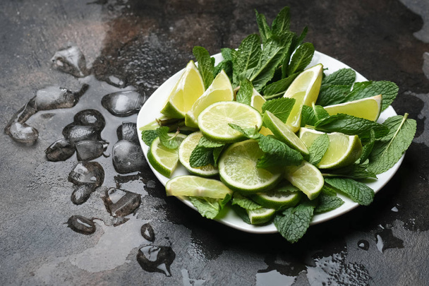 Ingredients for refreshing mojito cocktail  with mint, rum and lime, cold drink or beverage with ice on dark stone table, top view - Foto, afbeelding