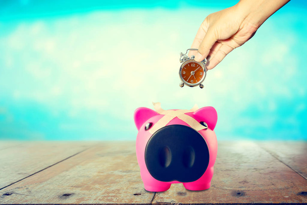 Hand with Alarm Clock in piggy bank on blurred  background - Photo, Image