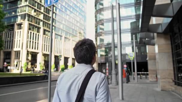 Atrás del hombre caminando por la calle y el centro de negocios de vidrio en una gran ciudad
 - Metraje, vídeo