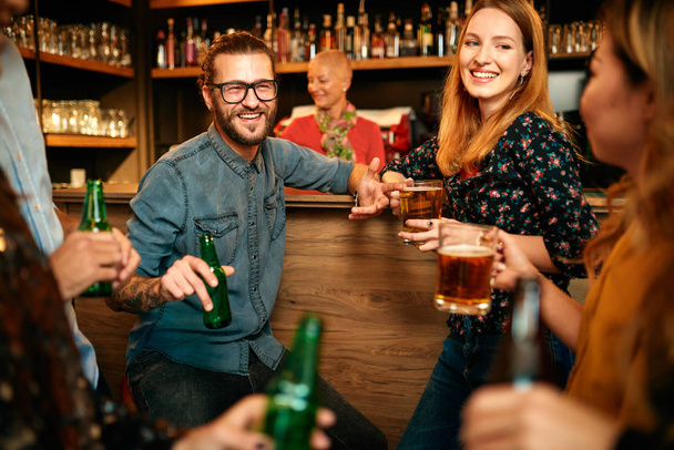 Grupo de amigos bebiendo cerveza, charlando y divirtiéndose en el pub. Noche fuera.
. - Foto, imagen