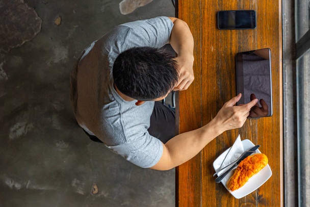 Muscoloso asiatico freelance utilizzando tablet mentre fa colazione in mensa
 - Foto, immagini