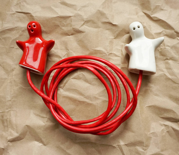 Подключение или отключение как концепция. Пара красных и белых керамических фигурок, соединенных с красной проволокой
 - Фото, изображение