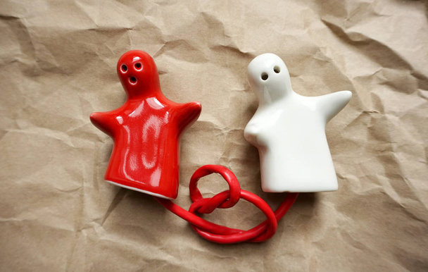 Par de duas figuras de porcelana na forma de pessoas amarradas a um fio vermelho amarrado em um nó
 - Foto, Imagem