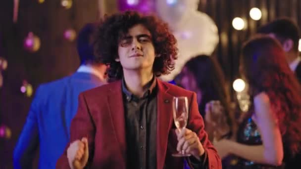 Bardzo charyzmatyczny facet z kręconymi włosami na wielkiej imprezie przed kamerą trzymający kieliszek szampana i cieszący się chwilą - Materiał filmowy, wideo