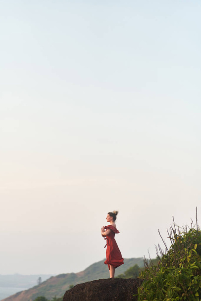 Young girl practices yoga in a red dress on a mountain in India - Photo, Image
