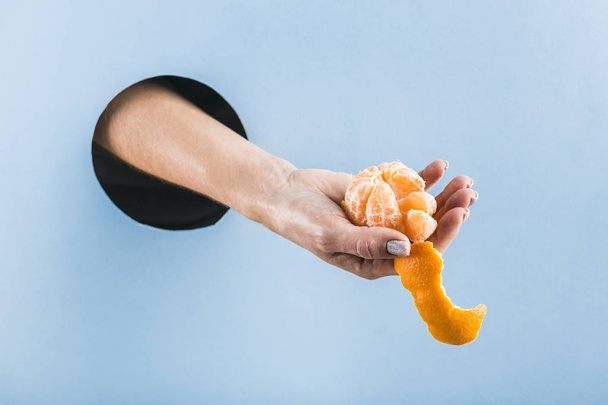 Женская рука вытаскивает полуочищенный мандарин из черной дыры
 - Фото, изображение