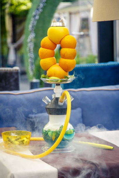 Hookah on the oranges. A hookah bowl consists of several oranges strung on top of each other.  The hookah flask is round and transparent, filled with blue-green liquor.  - 写真・画像
