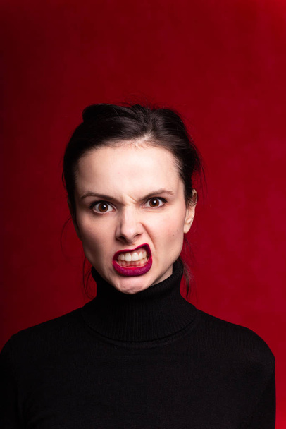 girl with red lipstick on the lips in a black turtleneck, red background - Фото, изображение