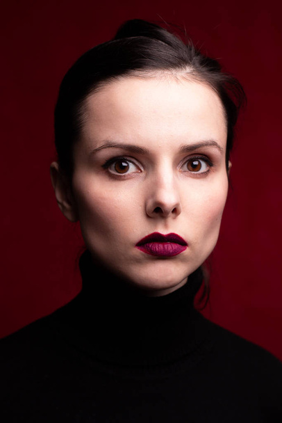 girl with red lipstick on the lips in a black turtleneck, red background - Fotografie, Obrázek