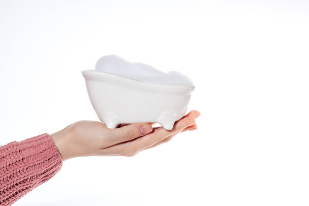 female hand holds a small bathtub filled with foam, the concept of cleanliness and body care - Photo, Image