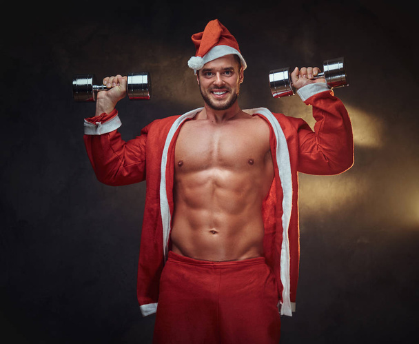 Handsome guy in Santa costume with dumbbells - Photo, Image