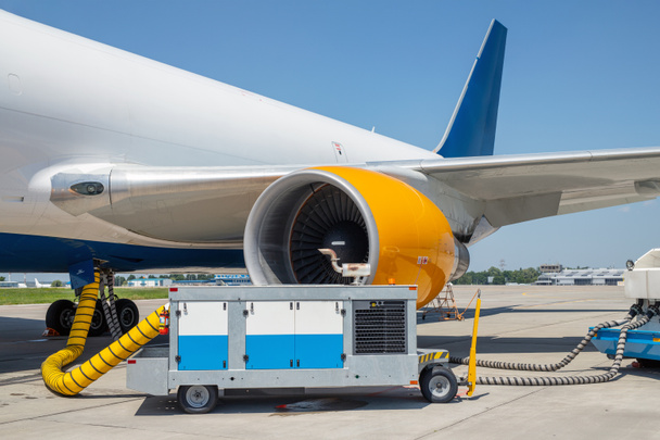 Big modern commercial cargo freight plane parked on airport runway and connected to ground supply power unit. Aircraft maintenance service and check-up before flight. Airport handling industry. - Photo, Image