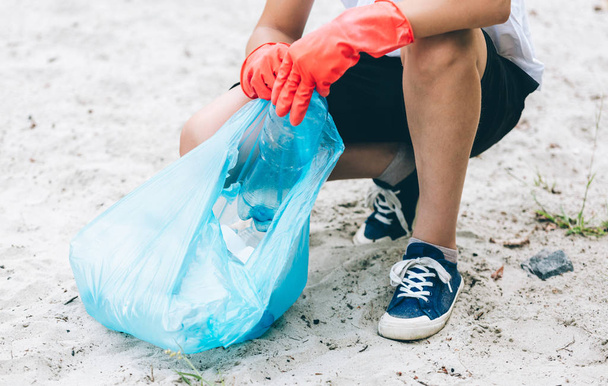 Volunteer boy picks up dirty plastic bottles in park. Hands collect garbage, pick up trash in bag. Eco activist cleaning up nature from plastic. - Photo, Image