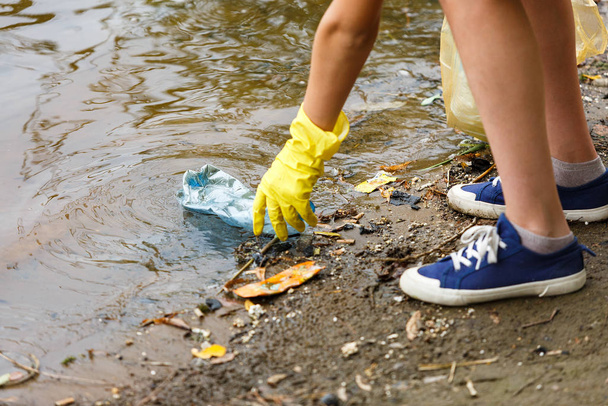 Junge in weißem T-Shirt und Handschuhen sammelt am Strand Müll und Plastikflaschen in blauen Verpackungen ein. junger Freiwilliger. Umweltschutz, Umweltschutzkonzept. Hände in Handschuhen - Foto, Bild