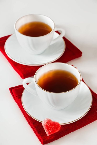 Kaksi valkoista teekuppia valkoisella pohjalla. Sydämen muotoinen marmeladi, ystävänpäivän ja rakkauden symboli. Kahden rakastavaisen tapaamisen käsite
. - Valokuva, kuva