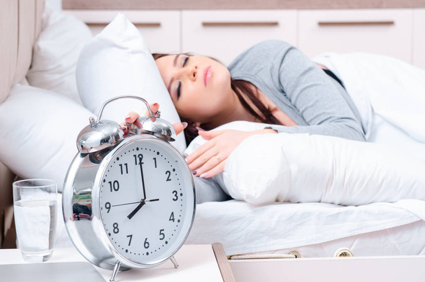 Giovane donna sdraiata sul letto nel concetto di gestione del tempo - Foto, immagini