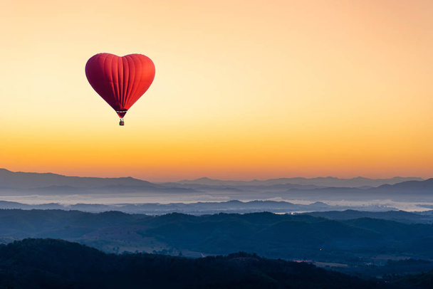 山の上を飛ぶ心臓の形をした赤い熱気球 - 写真・画像