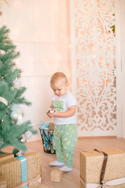 Cute little boy by the Christmas tree and fireplace decorated with garlands and gifts. Christmas mood - Valokuva, kuva