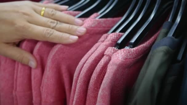 Las manos de la mujer corren a través de un estante de ropa y elige el suéter
. - Metraje, vídeo