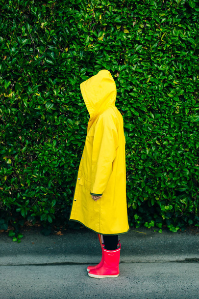 Sarı yağmurluklu kız arka planda çimenli bir duvarda - Fotoğraf, Görsel