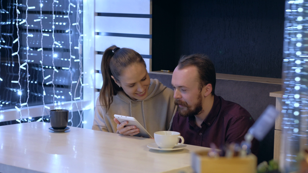 Egy pár ül egy kávézóban, beszélgetnek, kávéznak és nézik az okostelefonon..  - Felvétel, videó