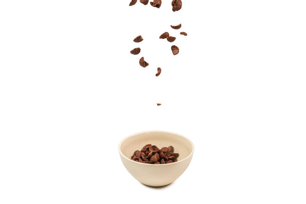 Copos de maíz de chocolate cayendo al tazón blanco aislado en whit
 - Foto, imagen