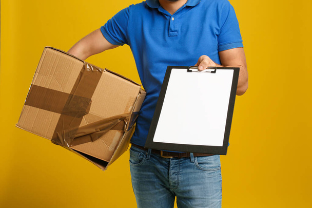 Courier with damaged cardboard box and clipboard on yellow backg - Photo, Image