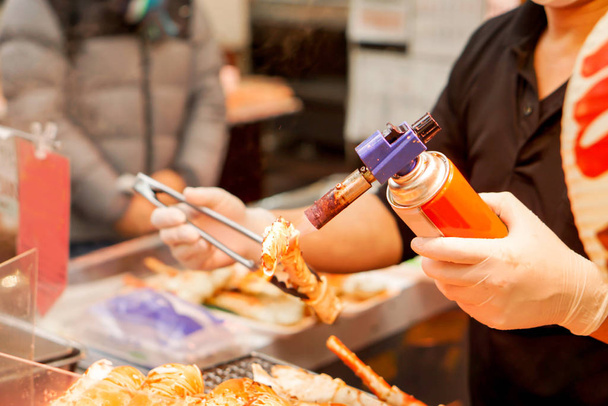 Main du chef en utilisant la cuisson brûleur et brûler pattes de crabe roi et crevettes géantes sur le poêle à vendre pour le client au marché Kuromon. King crabe jambes Bar-B-Q est populaire parmi les touristes qui viennent au Japon
. - Photo, image