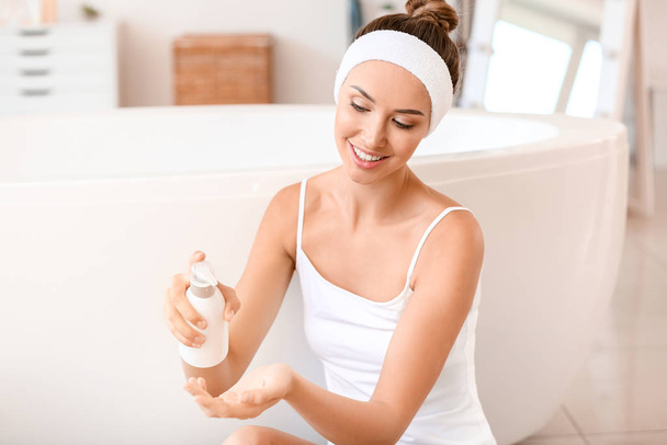 Beautiful young woman applying cream onto her skin in bathroom - Photo, Image
