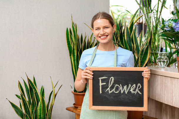 Portrait of female florist holding chalkboard with word FLOWER in shop - Fotó, kép