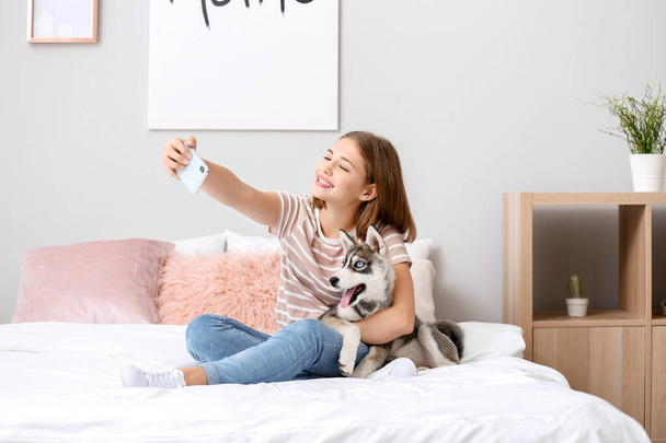 Cute teenage girl with funny husky puppy taking selfie on bed at home - Foto, immagini